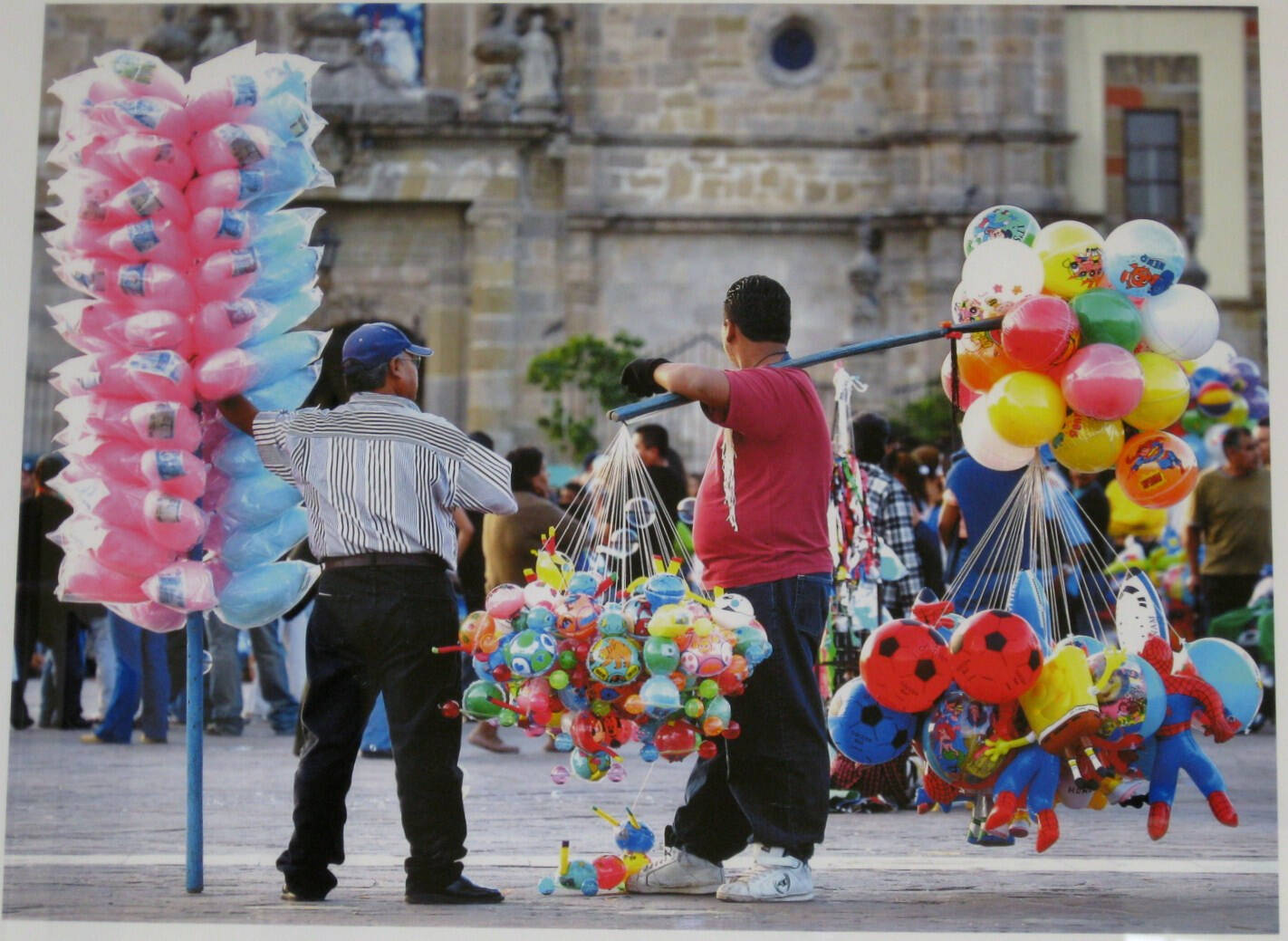 Image of men in Mexico vending goods in a plaza including plastic toys, balloons, and cotton candy.